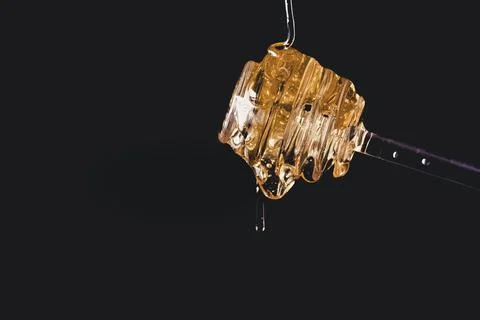 A honey spoon with the honey spilling out with black background. Stock Photos