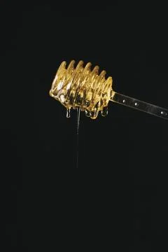 A honey spoon with the honey spilling out with black background. Stock Photos