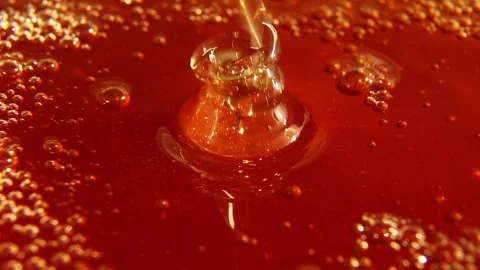 Honey stream hitting bubbling amber liquid surface Stock Footage 322663785