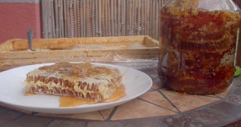 Honeycomb slice and jar of amber honey with moving shine on mosaic patio table Stock Footage 344598054
