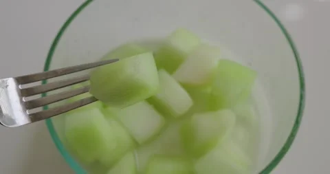 A honeydew melon chunk held on a fork above a glass bowl Stock Footage 330089290