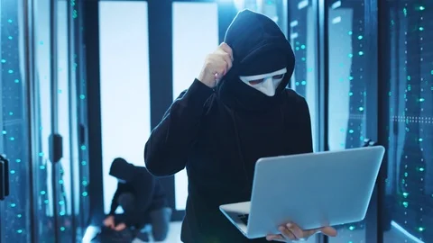 Hooded anonymous hacker coding on laptop noticing a mistake calling for his Stock Footage 120694328