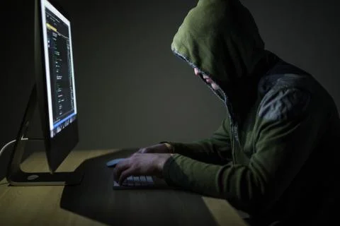 Hooded computer hacker stealing information with pc in Dark room background Stockfoto's