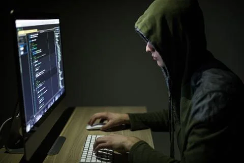 Hooded computer hacker stealing information with pc in Dark room background 写真素材