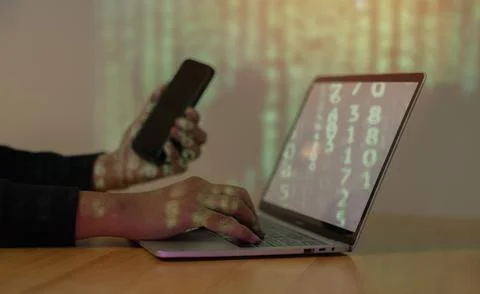 Hooded computer hacker use phone and stealing information with laptop. Stock-Fotos