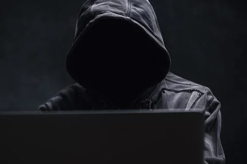 Hooded computer hacker using laptop computer Stock Photos