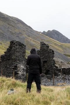A hooded figure, back to camera. Looking at a ruined building Stock Photos