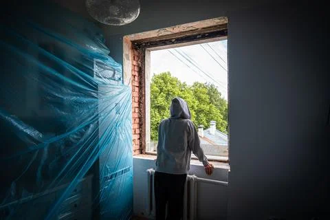 Hooded figure observes development of interior through open window Stock-Fotos