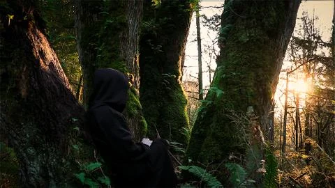 Hooded Figure Watching the Sunset in the Woods Stock Photos