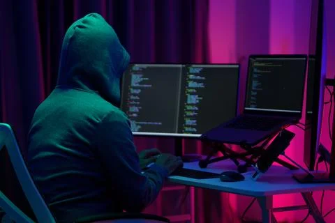 Hooded Hacker Coding at Dual Monitors in Dark Neon Room Stock Photos