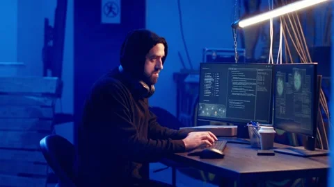 Hooded hacker creating pirating crack for software and video game releases Stock Footage 319520183