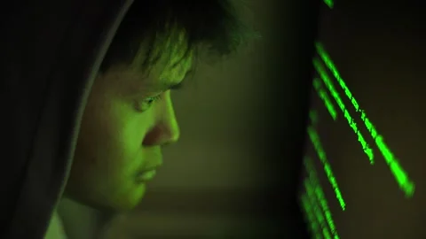 A hooded hacker in the dark night, lines of green code glowing bright Stock Footage 336187844
