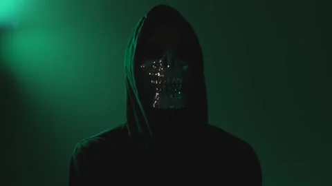 Hooded hacker with face mask staring at camera in dark room Stock Footage 310359434