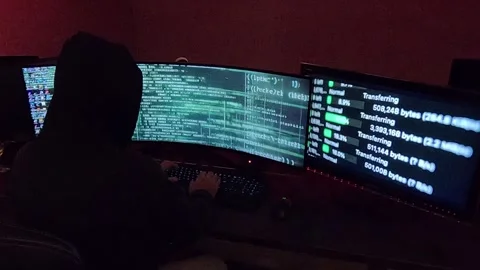 A hooded hacker programs lines of code in a dark, shadowy atmosphere. Stock Footage 283592460