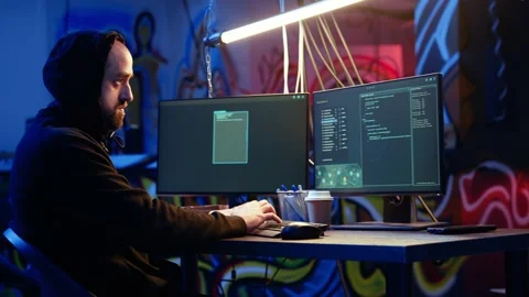 Hooded hacker running code in graffiti painted basement Stock Footage 319518118
