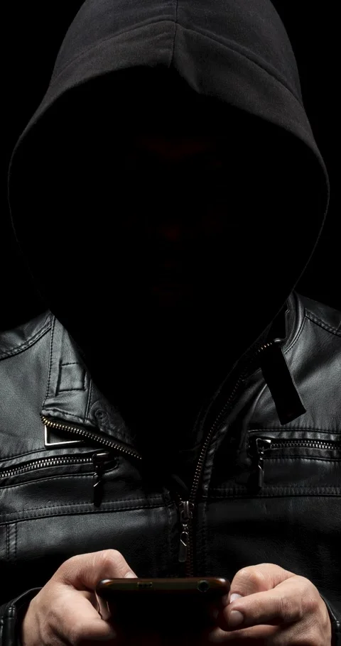 Hooded hacker in the shadows using an smartphone with his both hands Video stock 328319858