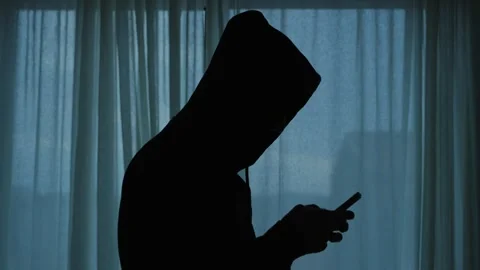 Hooded hacker silhouette using a smartphone for cybercrime Stockbeeldmateriaal 339303119