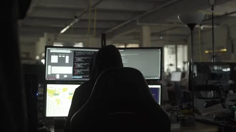 Hooded Hacker Sitting in Front of Computer Screens in Dark Office Stock Footage 344625036