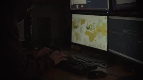 Hooded Hacker Typing on Keyboard in Dark Room with Monitors Stock Footage 344625496