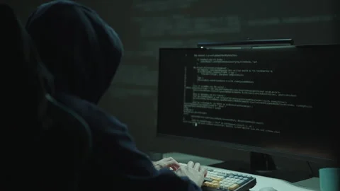 Hooded hacker typing on keyboard, with lines of code visible on computer monitor Stock Footage 324865548