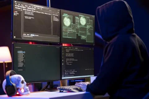 Hooded hacker in underground HQ coding malware to exploit network backdoors Stock Photos