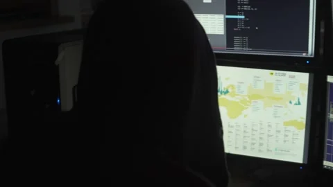 Hooded Hacker Working on Multiple Computer Monitors in Dark Room Stock Footage 344624378