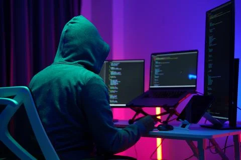 Hooded Hacker Working at Multiple Monitors in Dark Room 写真素材