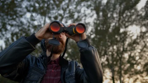 Hooded hipster bearded young man is looking through binoculars. Stock Footage 119042003
