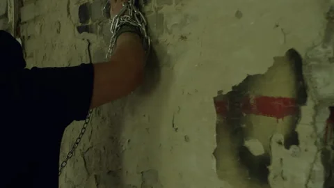 Hooded man breaking a decaying wall with chained hands Stock Footage 301328021