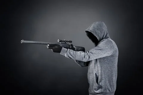Hooded man with rifle over dark misty background Stock Photos