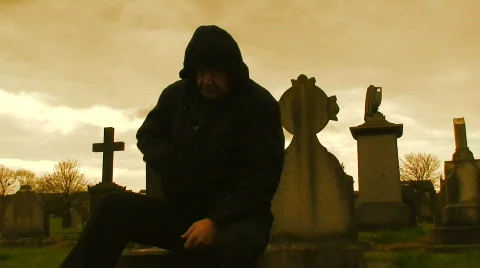 Hooded man sitting amongst gravestones Stock Footage