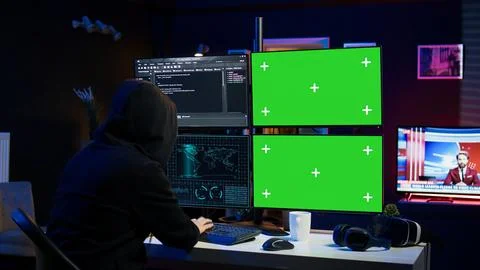 Hooded man writing lines of code on green screen PC from apartment Stock Photos