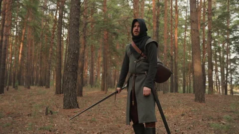 Hooded medieval archer pausing with bow and quiver in pine forest clearing Stock Footage 343685753