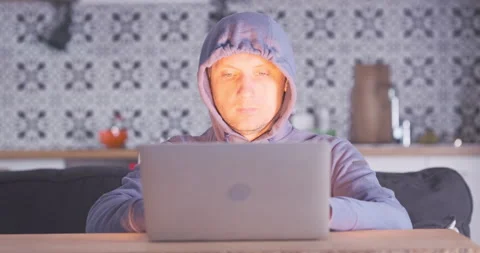 Hooded programmer works on laptop at home. Front view, bright light from Stock Footage 237678079