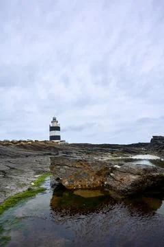 Hook lighthouse with foreground rocks and cloudy sky. Wexford, Ireland. Stock Photos