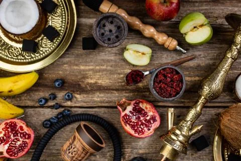 Hookah components on a rustik old wood table with fruits, tobacco and cocoa c Stock Photos