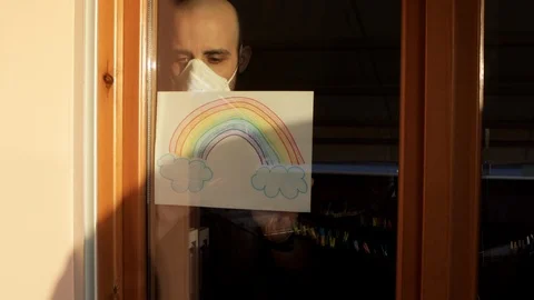 Hope concept: young man behind the window with virus mask and rainbow drawing Stock Footage 126781835