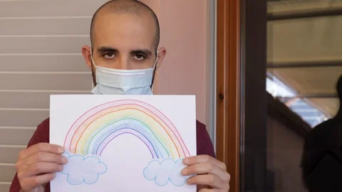 Hope concept: young man with virus mask and rainbow drawing is sad, then smiles Video stock 128952910