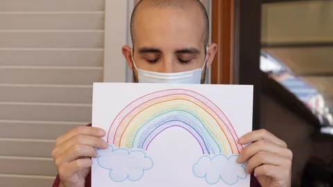 Hope concept: young man with virus mask and rainbow drawing is sad Video stock 128953337