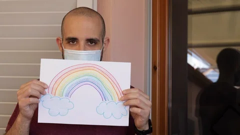 Hope concept: young man with virus mask and rainbow drawing is sad, then smiles Video stock 128953394