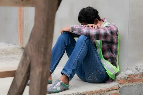 Hopeless builder worker sitting in construction site bend head down in his .. Stock Photos