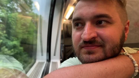 Horizontal 4K video close up. Man seat and looks out of large train window Stock Footage 312628620