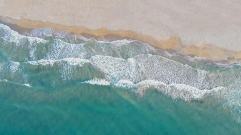 Horizontal aerial top down view of turquoise ocean waves washing on a sandy.. Stock Photos