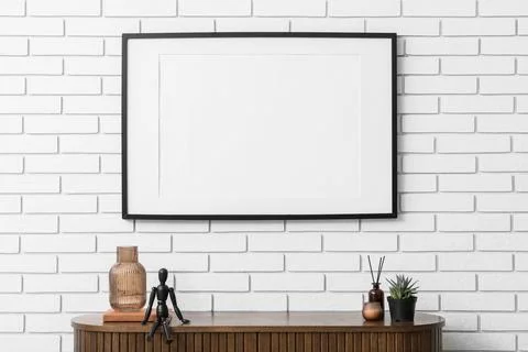 Horizontal black frame mockup on a white brick wall with a wooden cabinet and Stock Photos