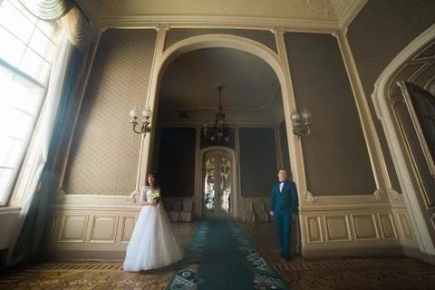 The horizontal full-length view of the happy newlyweds standing near the walls Stock Photos