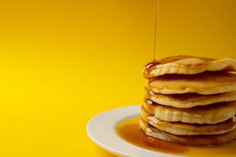 Horizontal image of maple syrup pouring onto stack of pancakes, yellow Foto stock