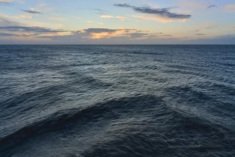 A horizontal oriented photograph of sea waves under an early morning sunrise sky Stock Photos