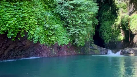 Horizontal pan shot of a hidden emerald lagoon and cave waterfall in Bali Stock Footage 336904289
