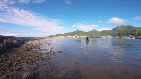 Horizontal pane view of sandy rocky bay area in Avatiu Harbor look out to boats  Stock Footage 258444394