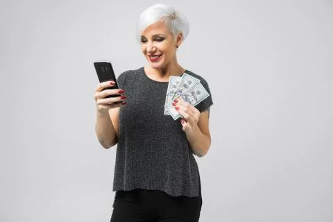 Horizontal portrait of adult blonde woman with smartphone and batch of money Stock Photos